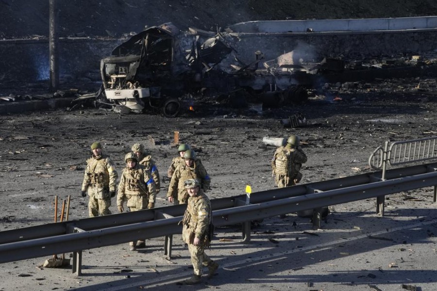 Ukrainian soldiers walk past debris of a burning military truck on a street in Kyiv, Ukraine, Saturday, Feb. 26, 2022. Russian troops stormed toward Ukraine's capital Saturday, and street fighting broke out as city officials urged residents to take shelter. (AP Photo/Efrem Lukatsky)