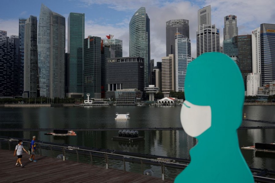 People wearing face masks pass a sign put up to encourage social distancing during the coronavirus disease (COVID-19) outbreak, at Marina Bay in Singapore, September 22, 2021. REUTERS/Edgar Su/File Photo