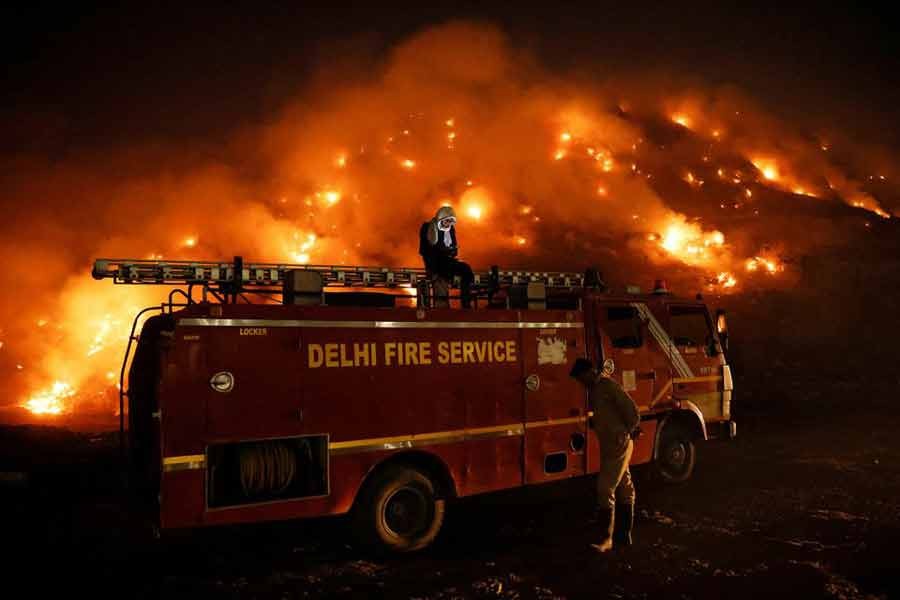 A firefighter using his mobile phone as he sits on top of a fire truck as smoke billows from burning garbage at the Bhalswa landfill site in New Delhi of India on Wednesday –Reuters photo