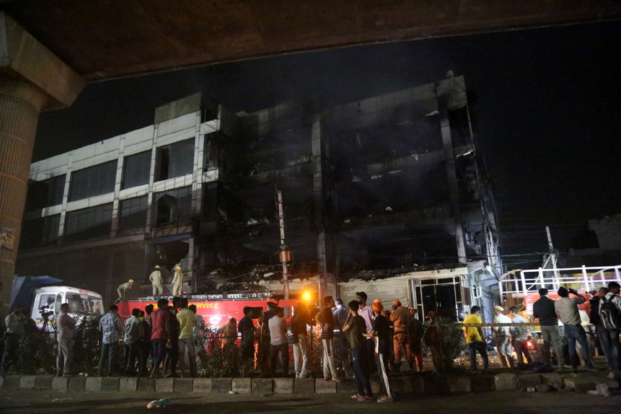 Rescue members and onlookers stand as fire fighters douse a fire that broke out at a commercial building in Delhi's western suburb on May 13, 2022 — Reuters