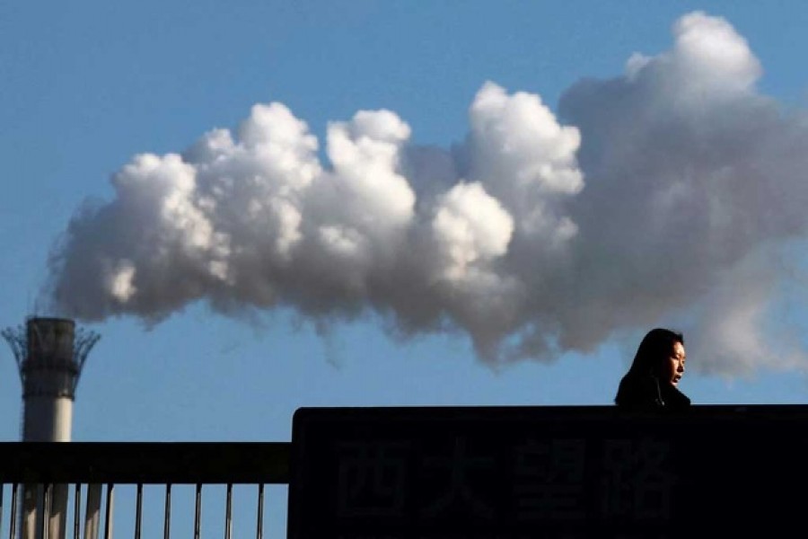 A woman walks across a bridge in front of a chimney billowing smoke from a coal-burning power station in central Beijing Feb 25, 2011. Reuters