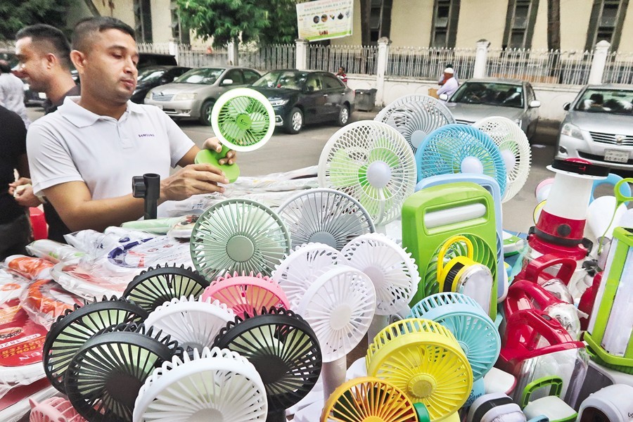 A customer is carefully examining a rechargeable fan at a makeshift shop on the footpath adjacent to Baitul Mukarram Market in Dhaka on Saturday. The sale of such fans and lamps has surged in recent times due to the scorching heat coupled with load shedding in capital and elsewhere — FE photo by Shafiqul Alam