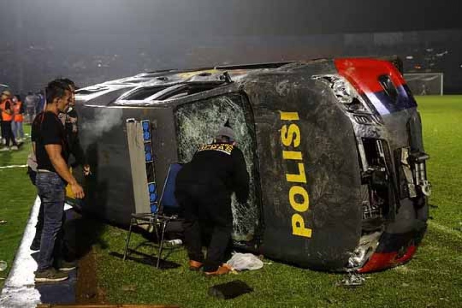 People stand next to a damaged car following a riot after the league BRI Liga 1 football match between Arema vs Persebaya at Kanjuruhan Stadium, Malang, East Java province, Indonesia, October 2, 2022, in this photo taken by Antara Foto. Antara Foto/H Prabowo/via REUTERS