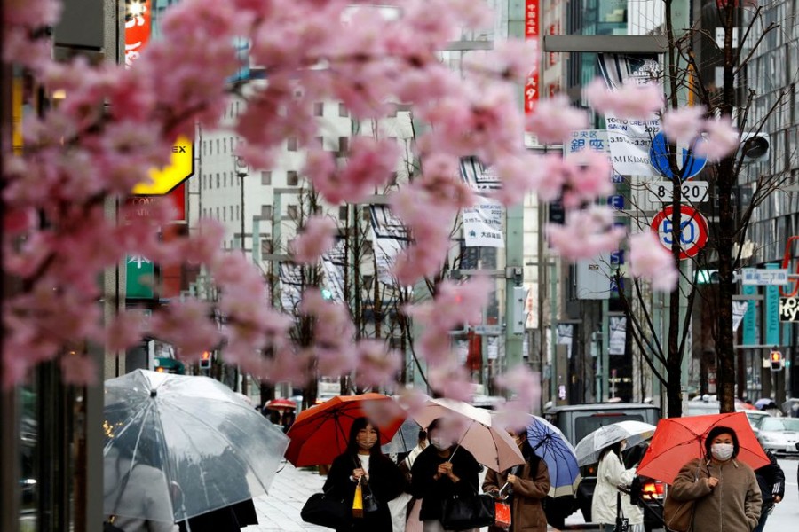 Pedestrians wearing protective face masks, amid the coronavirus disease (COVID-19) pandemic, are seen behind artificial cherry blossom decorations at a shopping district on the first day after the lifting of COVID-19 restrictions imposed on Tokyo and 17 other prefectures, in Tokyo, Japan, March 22, 2022. REUTERS/Kim Kyung-Hoon