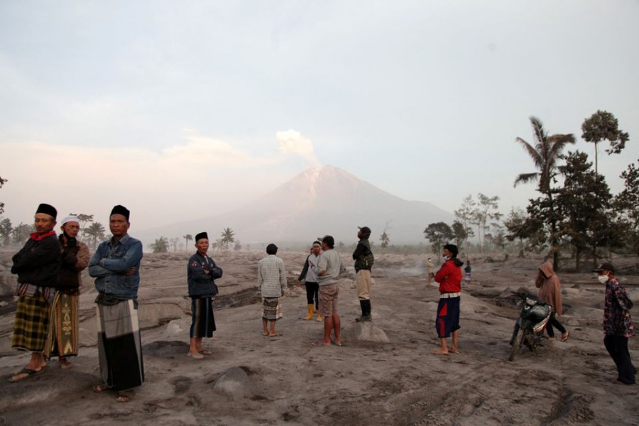 Villagers stand in an area covered with volcanic ash as Mount Semeru volcano erupts volcanic materials, as seen in the background in Sumberwuluh, Lumajang, East Java province, Indonesia on December 5, 2022, in this photo taken by Antara Foto — Antara Foto via Reuters