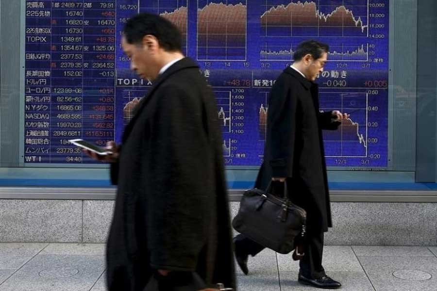 Men walk past an electronic board showing market indices outside a brokerage in Tokyo, Japan, March 2, 2016. Reuters