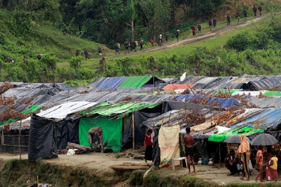 Rohingya refugees stand outside their temporary shelters at no man's land between Bangladesh-Myanmar border, as Myanmar security forces walk past a fence in Maungdaw, Myanmar Sept 9, 2017. Reuters