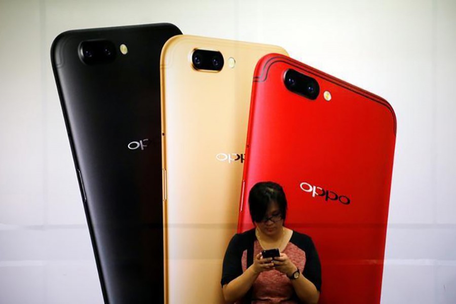 A woman uses her mobile phone next to an Oppo mobile handset advertisement in Singapore August 7 last. - Reuters