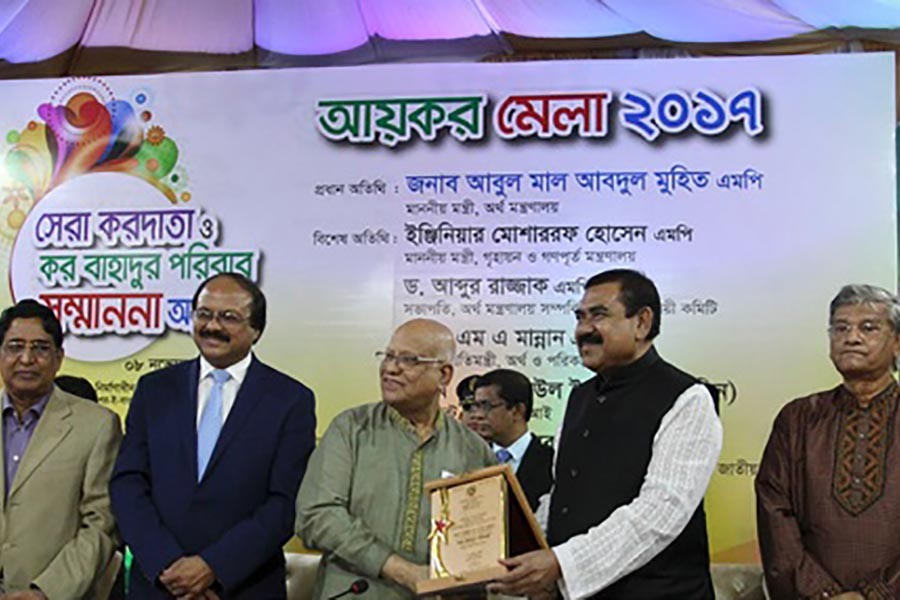 Finance Minister Abul Maal Abdul Muhith hands over certificate of ‘Kor Bahadur’ title at a programme on Wednesday. -bdnews24.com photo