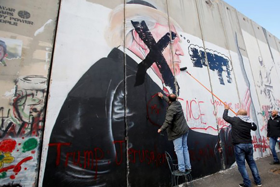 Palestinians damage a mural depicting US President Donald Trump on a part of the Israeli barrier in the West Bank city of Bethlehem on Thursday. - Reuters photo