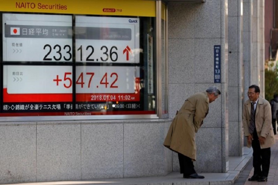Men exchange greetings in front of an electronic board displaying the Nikkei average outside a brokerage in Tokyo, Japan January 4, 2018. Reuters