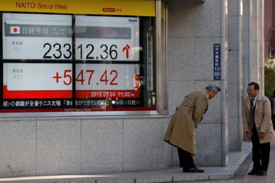 Men exchange greetings in front of an electronic board displaying the Nikkei average outside a brokerage in Tokyo, Japan January 4, 2018. Reuters