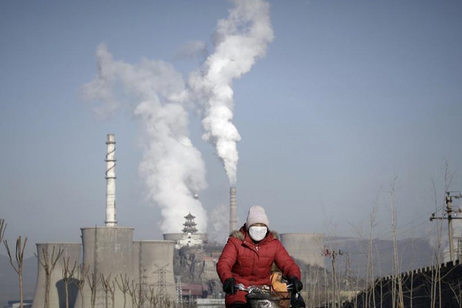 A woman wearing a mask rides past smoking chimneys and cooling towers of a steel plant in Beijing on January 17, 2013. - Reuters file photo
