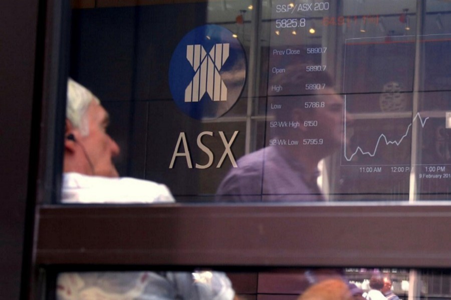 A pedestrian is reflected in a window where an investor sits looking at a board displaying stock prices at the Australian Securities Exchange (ASX) in Sydney, February 9, 2018. Reuters/File Photo