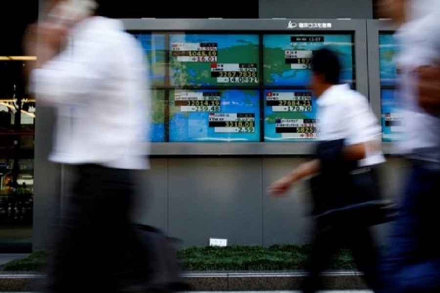 People walk past an electronic board showing Japan's Nikkei average outside a brokerage at a business district in Tokyo, Japan August 9, 2017. Reuters/Files