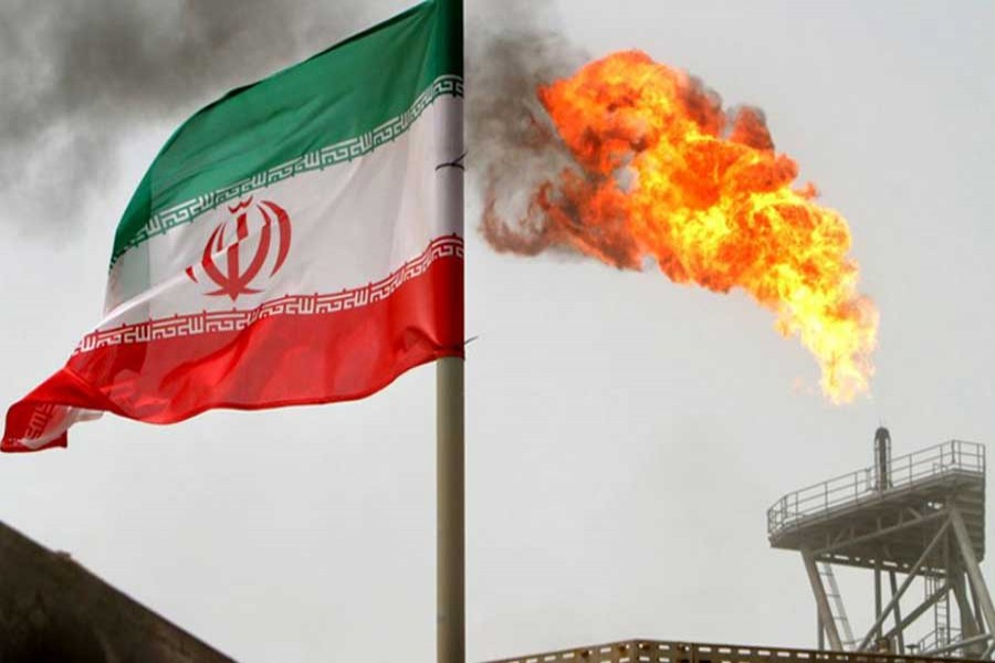 A gas flare on an oil production platform in the Soroush oil fields is seen alongside an Iranian flag in the Persian Gulf, Iran, July 25, 2005. Reuters/File Photo