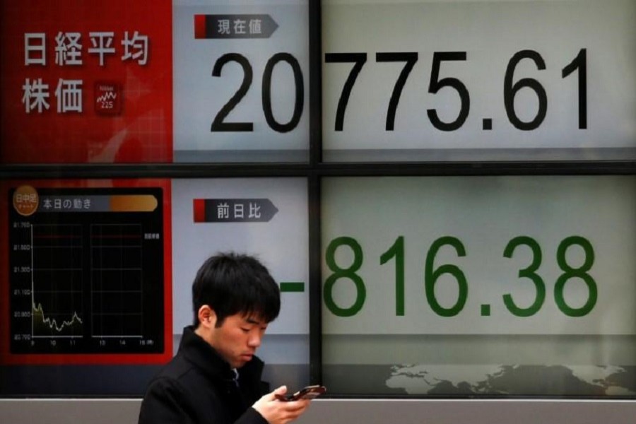 A man looks at a mobile phone in front of an electronic board showing Japan's Nikkei average outside a brokerage in Tokyo, Japan, March 23, 2018. Reuters/File Photo