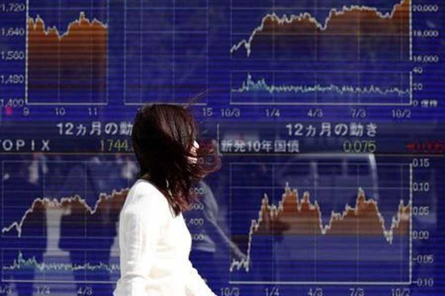 A woman walks in strong wind caused by Typhoon Lan, past an electronic board showing the graphs of the recent movements of Japan's Nikkei average outside a brokerage in Tokyo, Japan, October 23, 2017. Reuters/Files