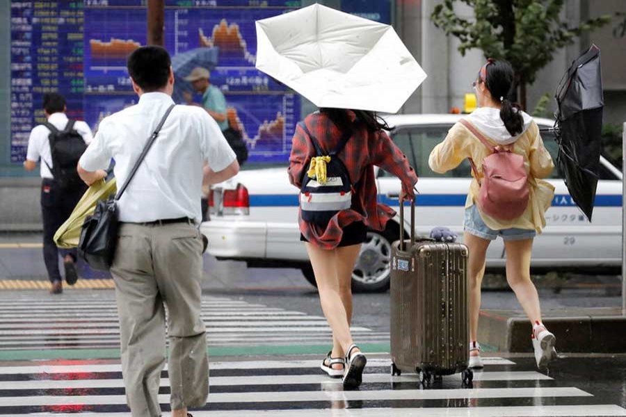 Passersby using umbrellas struggle against a heavy rain and wind in front of an electronic stock quotation board as Typhoon Shanshan approaches Japan's mainland in Tokyo, Japan, August 8, 2018. Reuters/Files
