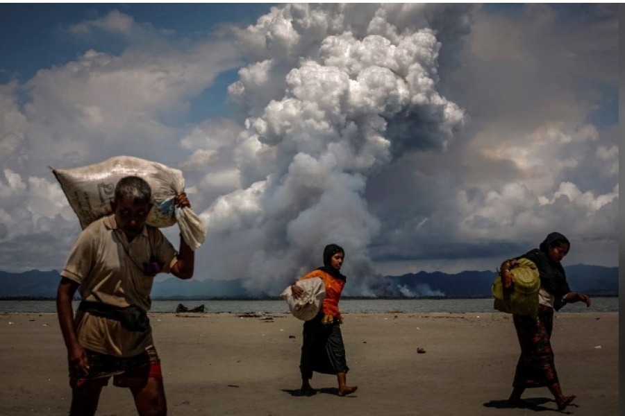 Smoke is seen on the Myanmar border as Rohingya refugees walk on the shore after crossing the Bangladesh-Myanmar border by boat through the Bay of Bengal, in Shah Porir Dwip, Bangladesh September 11, 2017. - Reuters