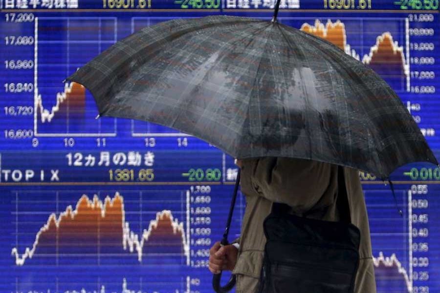 A pedestrian holding an umbrella walks past an electronic board showing the graphs of the recent fluctuations of Japan's Nikkei average outside a brokerage in Tokyo, Japan, January 18, 2016. Reuters/File Photo