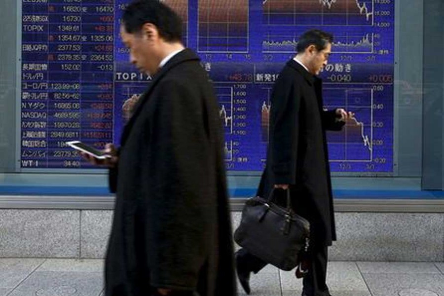 Men walk past an electronic board showing market indices outside a brokerage in Tokyo, Japan, March 2, 2016. Reuters/File Photo