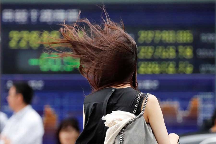 A woman struggles against strong wind caused by Typhoon Jebi, in front of an electronic stock quotation board in Tokyo, Japan, September 4, 2018. Reuters