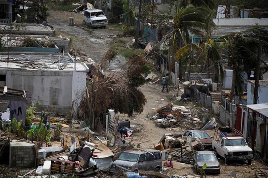 A man carrying a water container walks next to damaged houses after the area was hit by Hurricane Maria in Canovanas, Puerto Rico, September 26, 2017. Reuters/Files