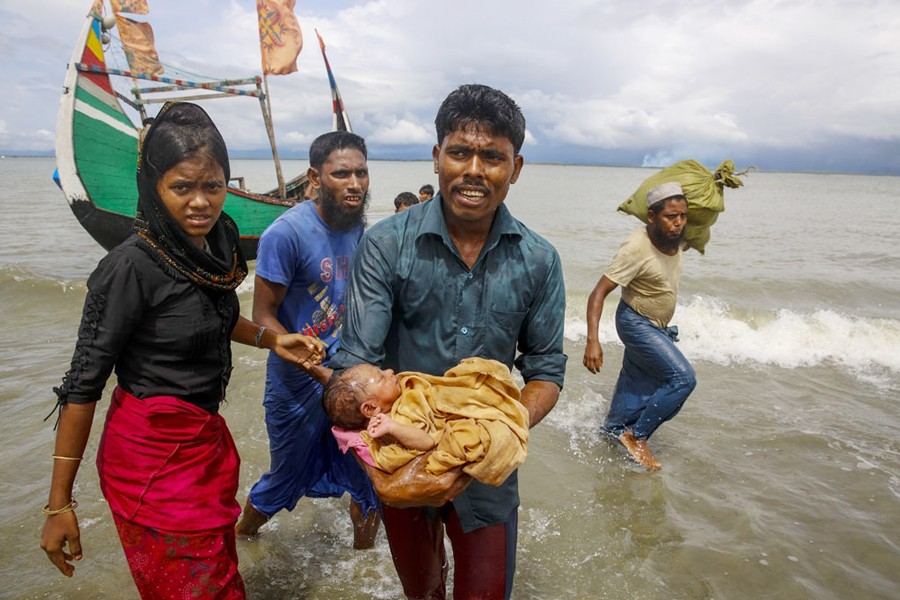 A file photo showing a Rohingya man carrying an infant to the shore from a boat that arrived at Shah Porir Dwip in Bangladesh from Rasidong in Myanmar recently. A US government investigation has found that Myanmar's military waged a planned, coordinated campaign of mass killings, gang rapes and other atrocities against the Southeast Asian nation's Rohingya Muslim minority	— Reuters