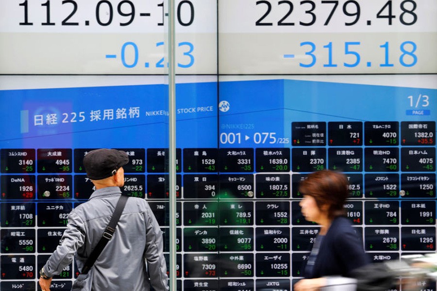 People walk past an electronic board showing Japan's Nikkei average (top R) and Japanese yen's exchange rate against the US dollar outside a brokerage in Tokyo, Japan, October 15, 2018. Reuters