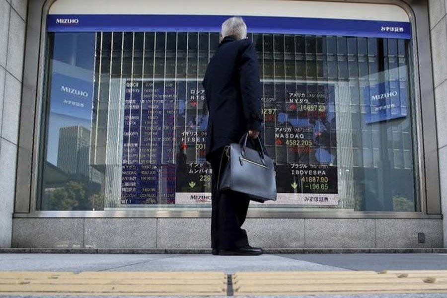 A pedestrian stands to look at an electronic board showing the stock market indices of various countries outside a brokerage in Tokyo, Japan, February 26, 2016. Reuters/Files
