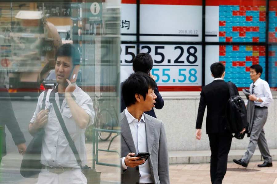 People walk past an electronic board showing Japan's Nikkei average outside a brokerage in Tokyo, Japan, October 12, 2018. Reuters/Toru Hanai
