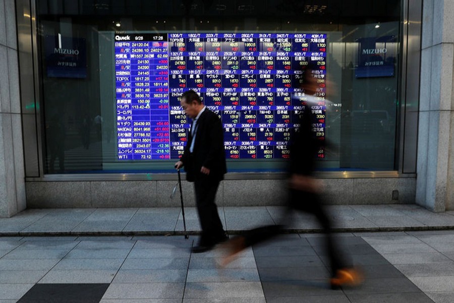 Passersby walk past in front of an electronic stock quotation board outside a brokerage in Tokyo, Japan, September 28, 2018. Reuters/Files