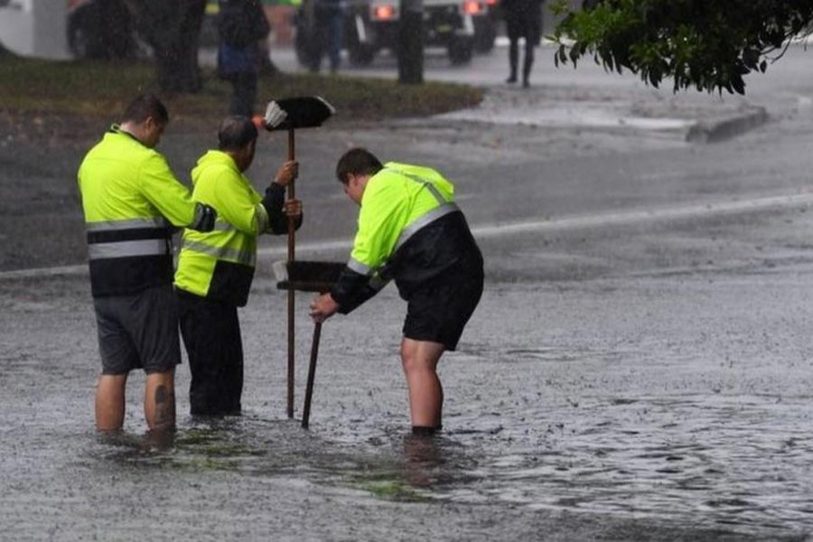 SYDNEY: Workers attempting to clear a drain in a water-logged road   	— EPA