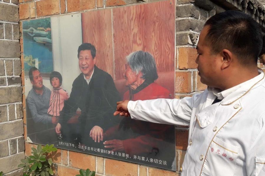 Yan Qing Guan pointing his finger at a photo of China President Xi Jinping and his family members in a photo on the wall of his business outlet in a Lankao village