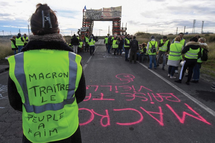MACRON IS A BELLWETHER, BECAUSE WHAT HAPPENS IN FRANCE WILL NOT STAY IN FRANCE: A Yellow vests (Gilets jaunes) protester with the words written on the back of her vest that read, 'Macron (referring to the French President) traitor, the people are hungry' blocks the road leading to the Frontignan oil depot in the south of France, as they demonstrate against the rise in fuel prices and the cost of living on December 03, 2018. 	—Photo: AFP