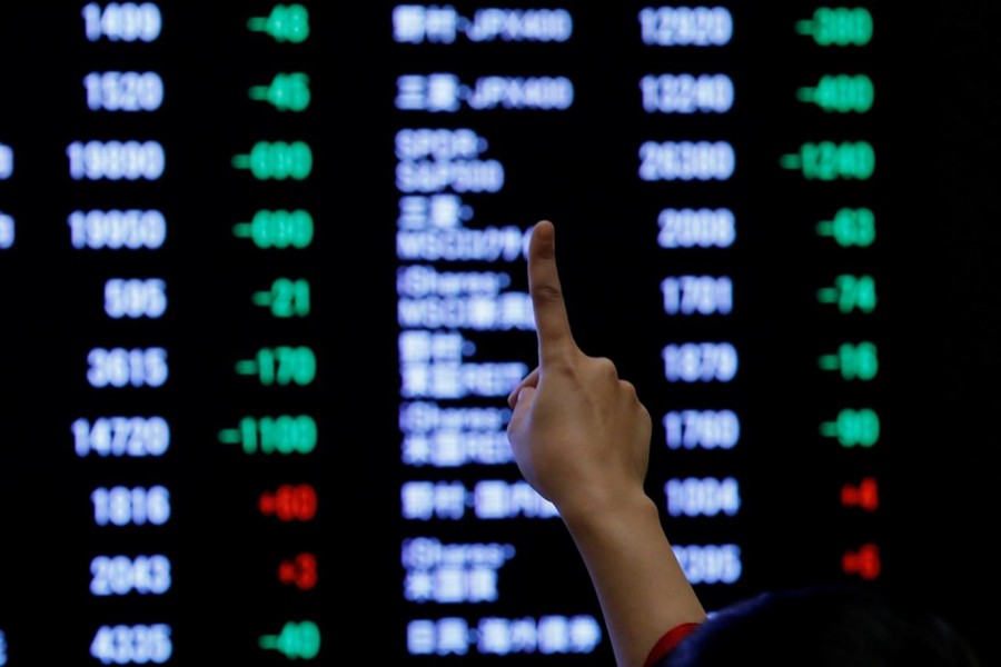 A woman points to an electronic board showing stock prices as she poses in front of the board at the Tokyo Stock Exchange (TSE), January 4, 2019. Reuters/File Photo