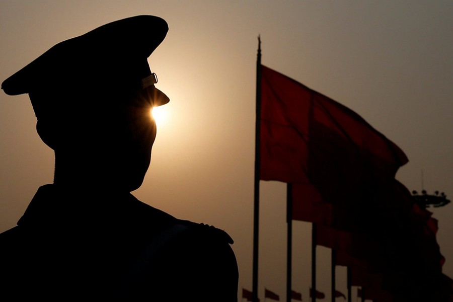 A China paramilitary police officer is seen silhouetted in front of flags — Reuters/File