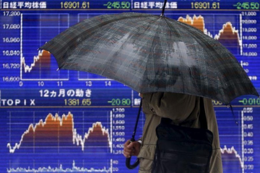 A pedestrian holding an umbrella walks past an electronic board showing the graphs of the recent fluctuations of Japan's Nikkei average outside a brokerage in Tokyo, Japan, January 18, 2016. Reuters/Files