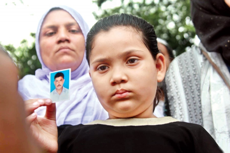 A girl showing the photograph of her father as relatives of the victims who were killed, injured and affected in the Churihatta fire, formed a human chain in front of Jatiya Press Club in the city on Friday demanding compensation — Focus Bangla