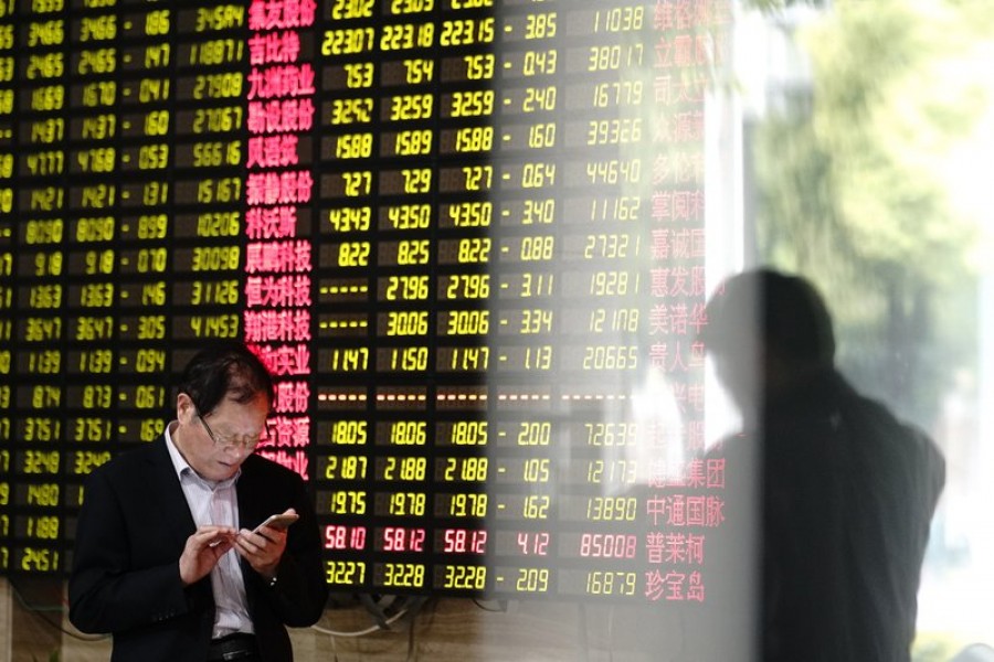 A man looks at his smartphone near a display showing stock prices at a brokerage house in Shanghai Monday, May 6, 2019. China's benchmark Shanghai Composite index dives on US President Donald Trump threat of more China tariffs. At right is a reflection off a display board. Photo: AP