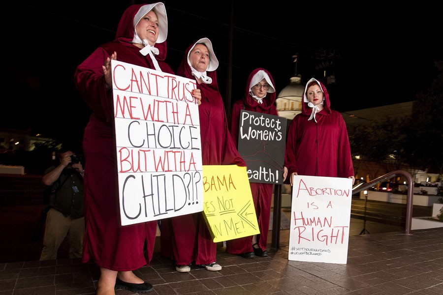 Anti-abortion ban bill protesters, dressed as handmaids, from left, Bianca Cameron-Schwiesow, Kari Crowe, Allie Curlette and Margeaux Hartline, wait outside of the Alabama statehouse after HB314, the near-total ban on abortion bill, passed the senate in Montgomery, Ala., on Tuesday, May 14, 2019. The measure now goes to Gov. Kay Ivey, who has not said whether she supports the measure - Mickey Welsh/The Montgomery Advertiser via AP