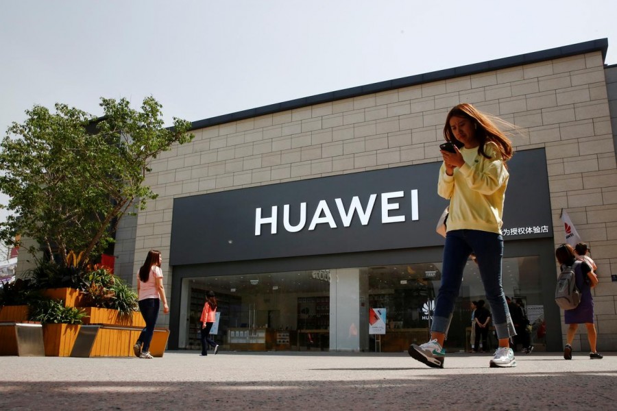 A woman looks at her phone as she walks past a Huawei shop in Beijing, China, May 16, 2019. Reuters/File Photo