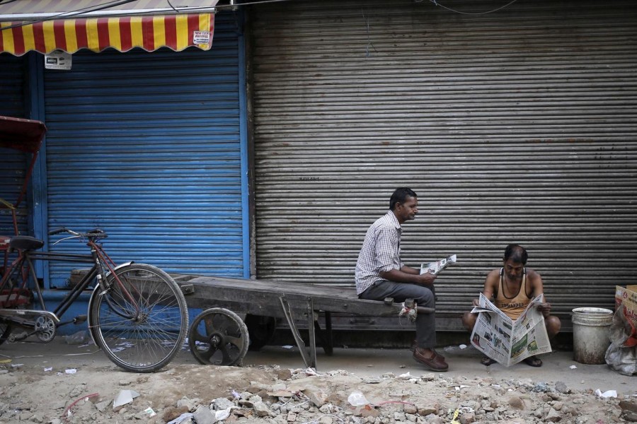 Labourers read newspapers in front of a closed shop in the old quarters of Delhi, India, March 29, 2016. Reuters/File Photo