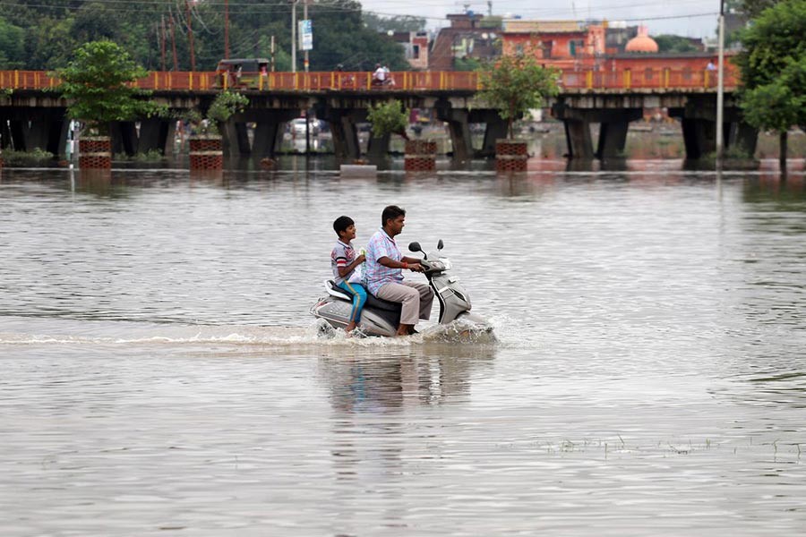 A man and a boy riding a scooter through a flooded road after heavy rains in Prayagraj, India, on Sunday. -Reuters Photo