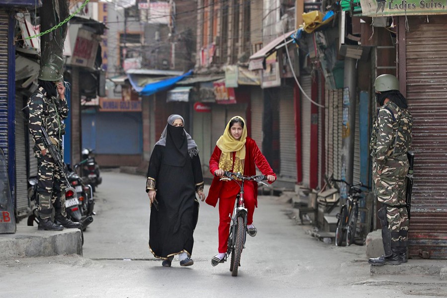 A Kashmir girl rides her bike past Indian security force personnel standing guard in front of closed shops in a street in Srinagar on October 30, 2019 — Reuters photo