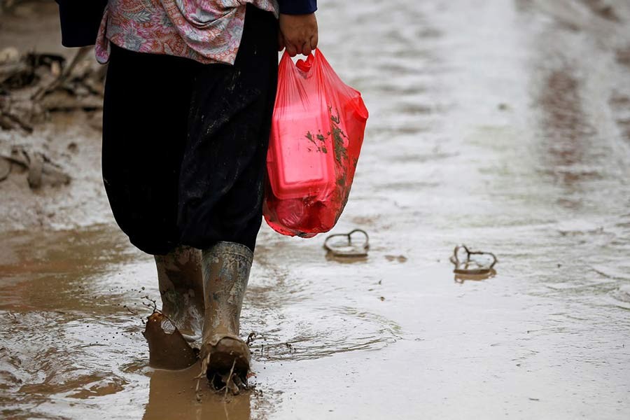A woman carrying a plastic bag containing food through the mud on a road after floods hit Bekasi, West Java province, Indonesia, on Friday. -Reuters Photo
