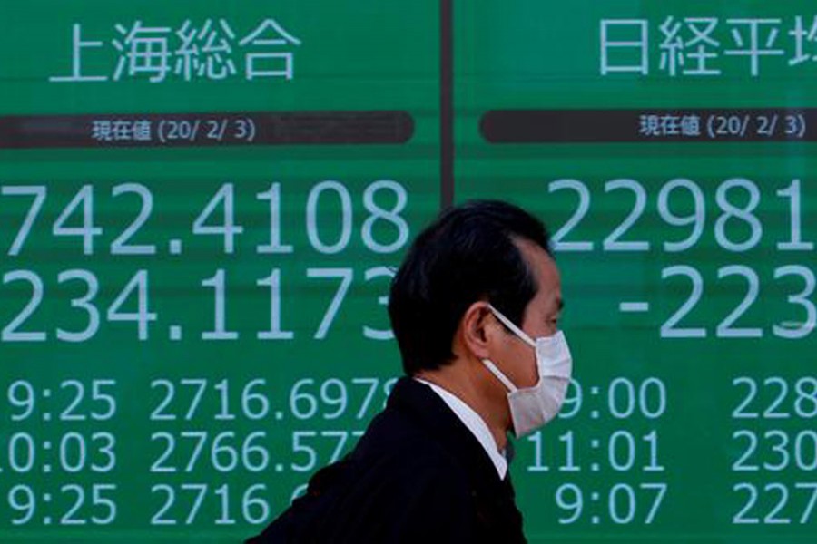 A man wearing a surgical mask stands in front of a screen showing Shanghai Composite index outside a brokerage in Tokyo, Japan, February 03, 2020 — Reuters