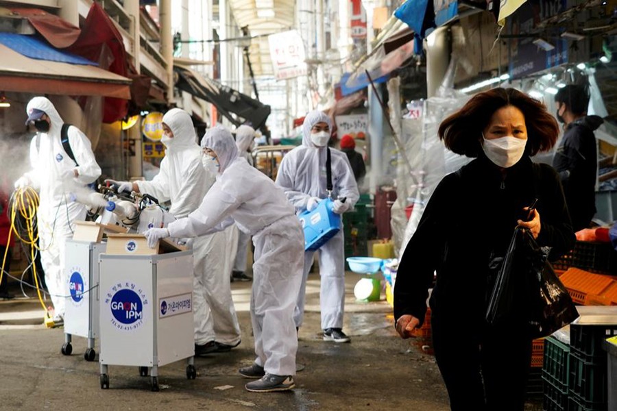 A woman wearing a mask to prevent contracting the coronavirus reacts as employees from a disinfection service company sanitise a traditional market in Seoul, South Korea, on February 26, 2020 — Reuters/Files