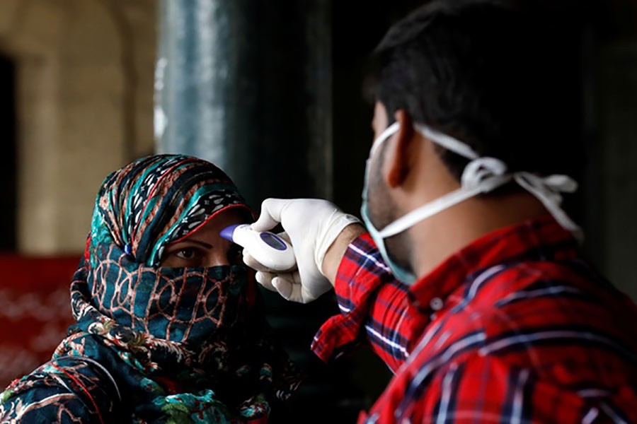 A health worker checking a woman's temperature amid coronavirus fears, at a counter at the Cantonment railway station in Karachi, Pakistan recently. -Reuters Photo